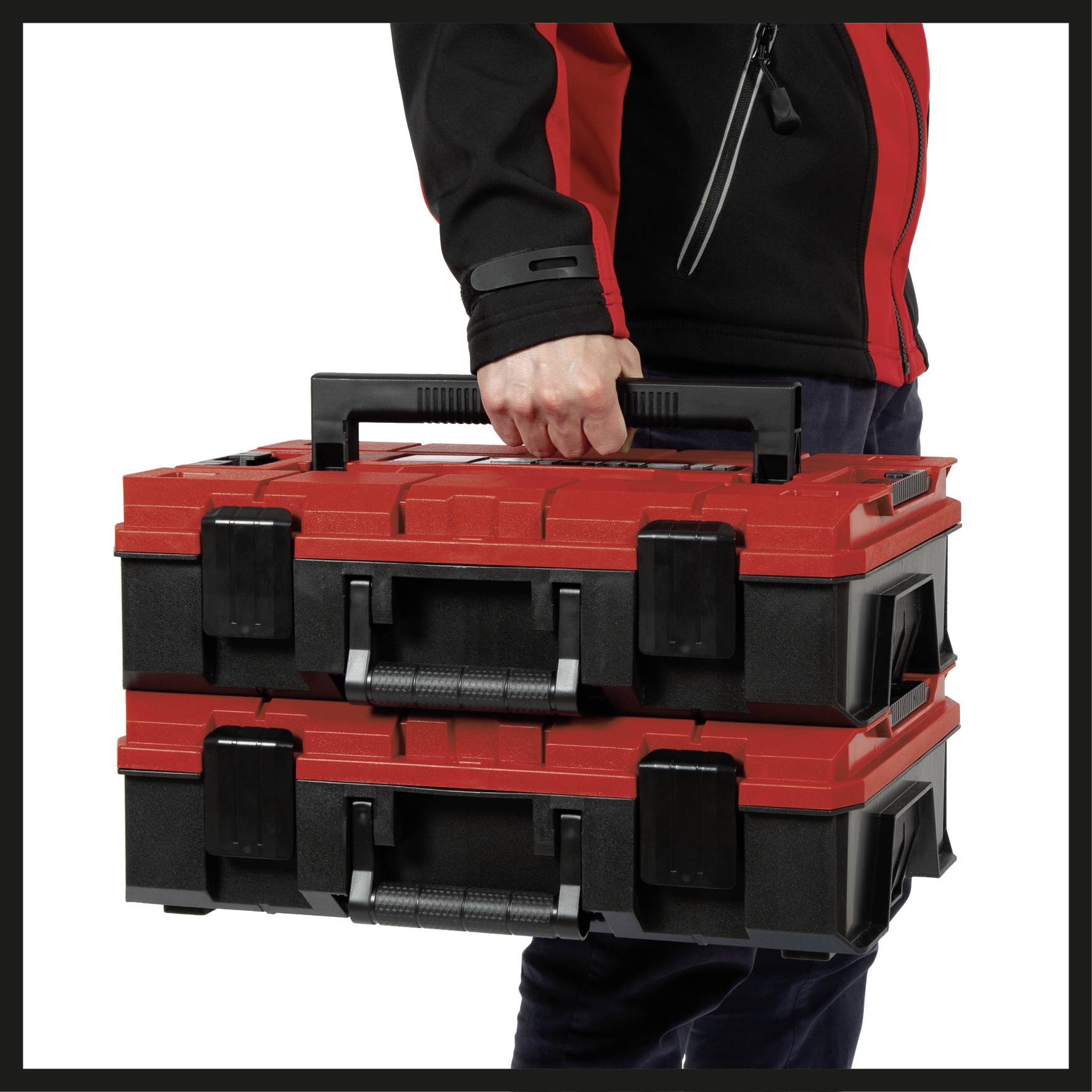 A person is carrying two stacked red and black toolboxes with handles.