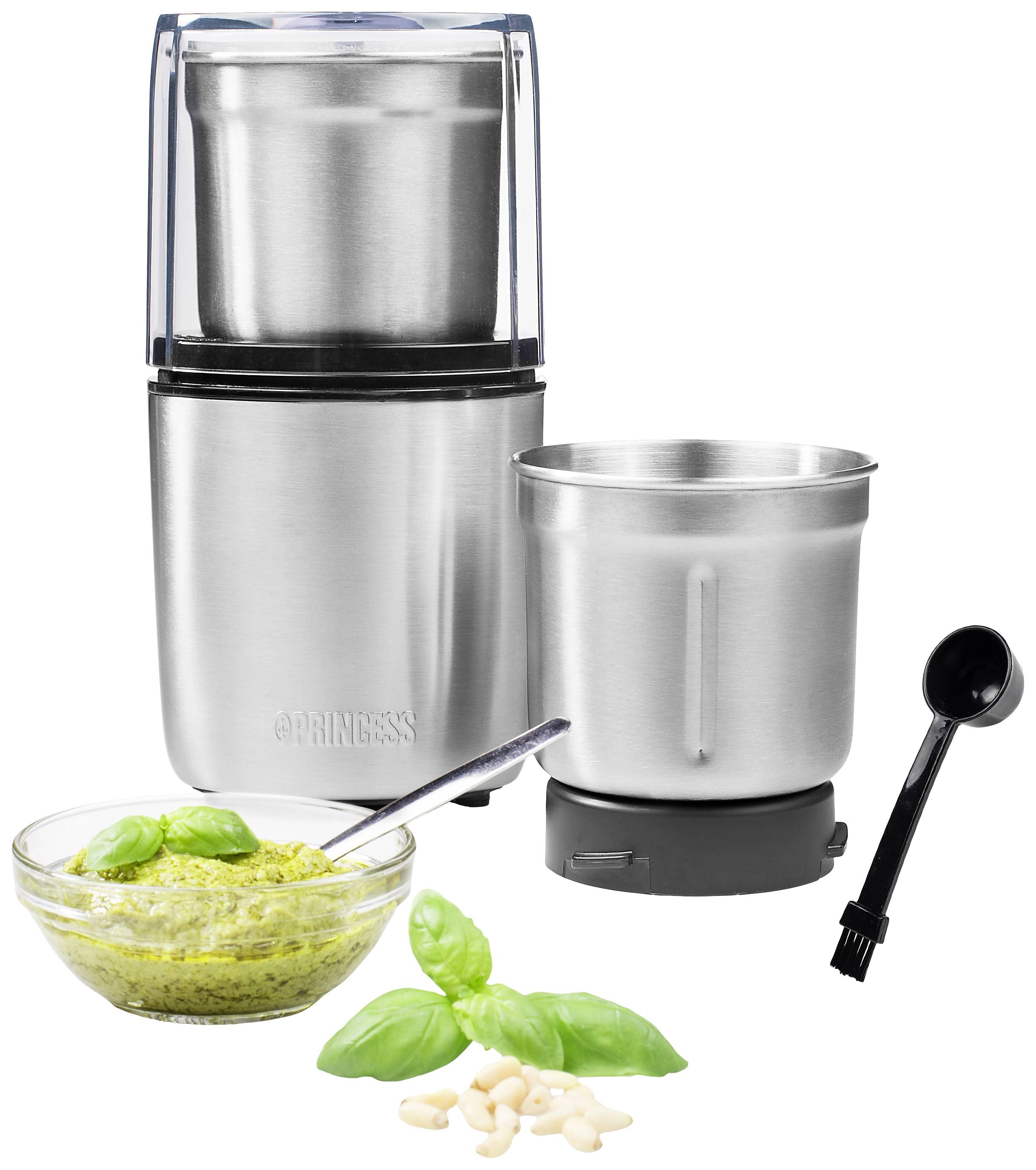 Stainless steel kitchen mill with two containers, placed next to a bowl of pesto, a spoon, and basil leaves on a white background.