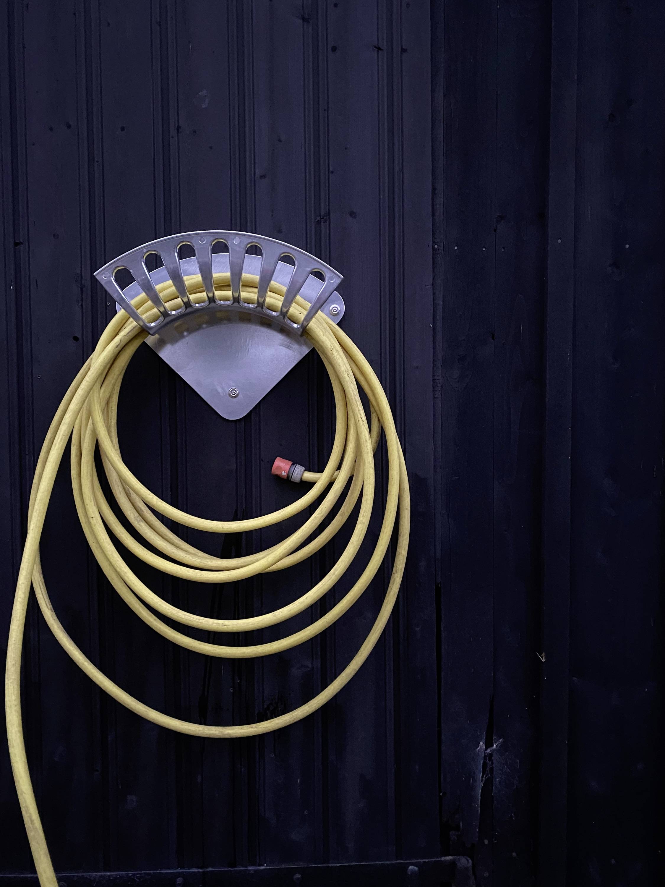A yellow garden hose hangs neatly on a grey wall bracket on a dark wooden wall.