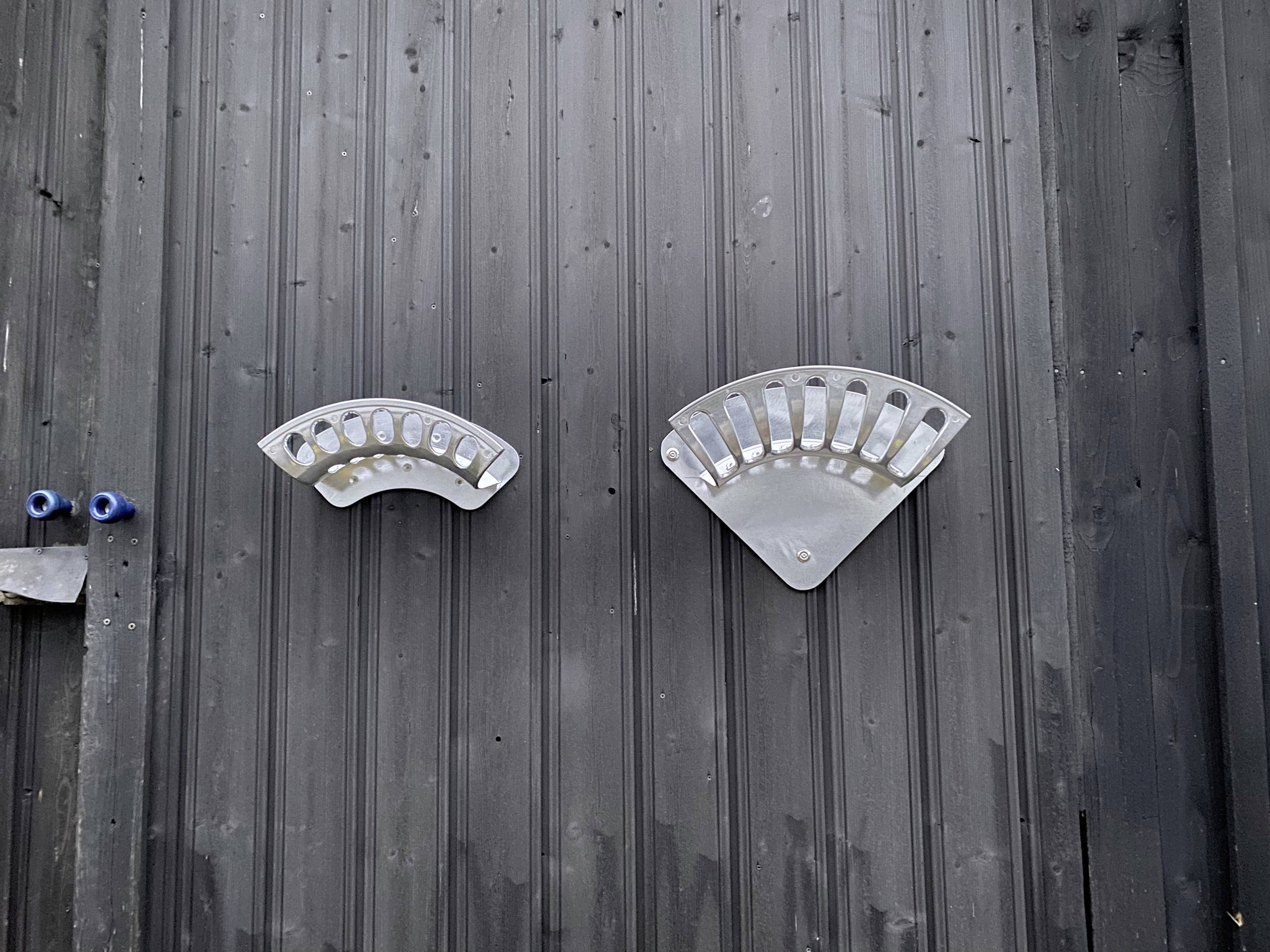 Two silver vent covers on a dark wall, arranged symmetrically side by side.