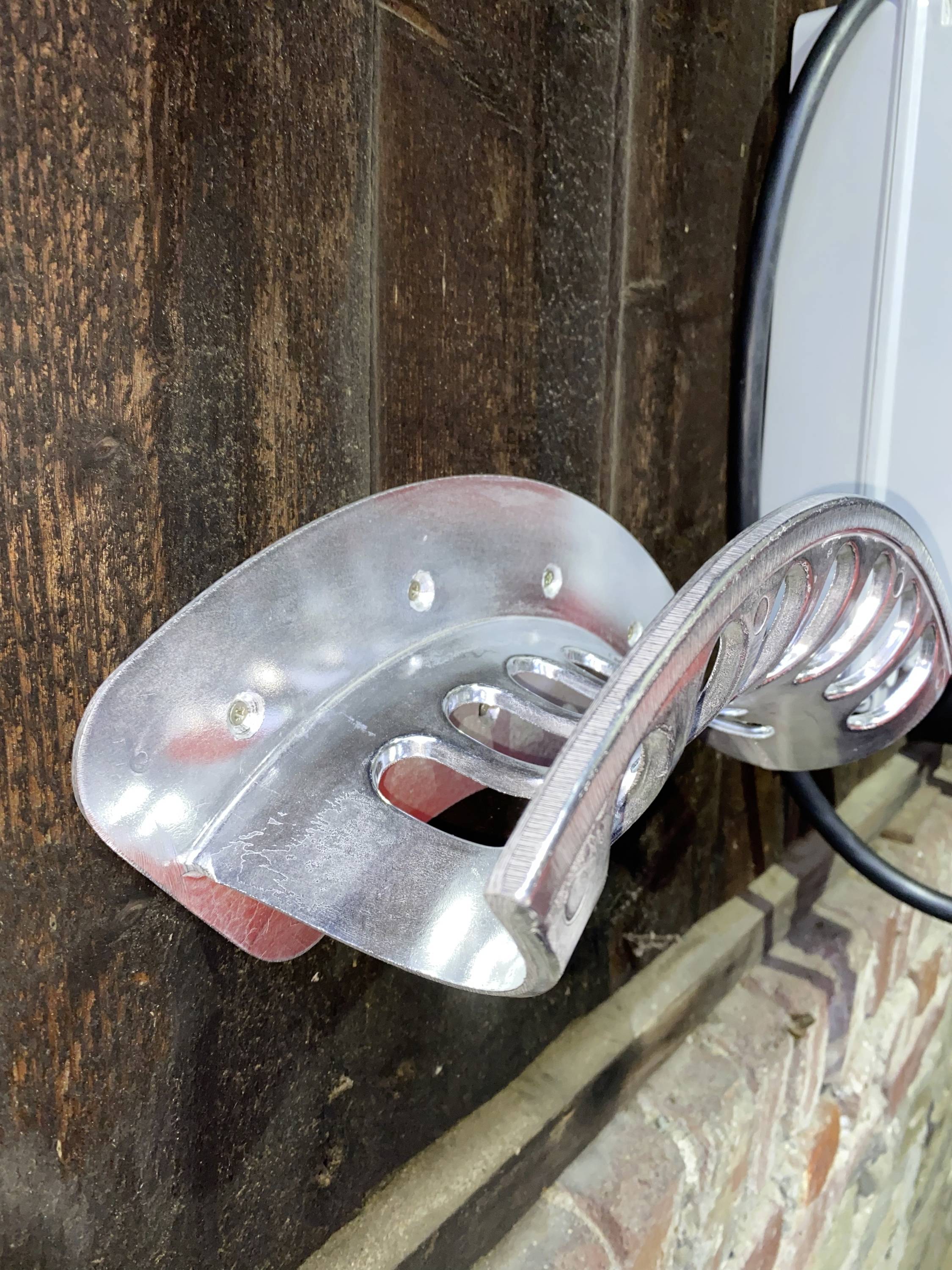 Metal bracket mounted on a wooden wall, presumably for hanging a bicycle, cables nearby.