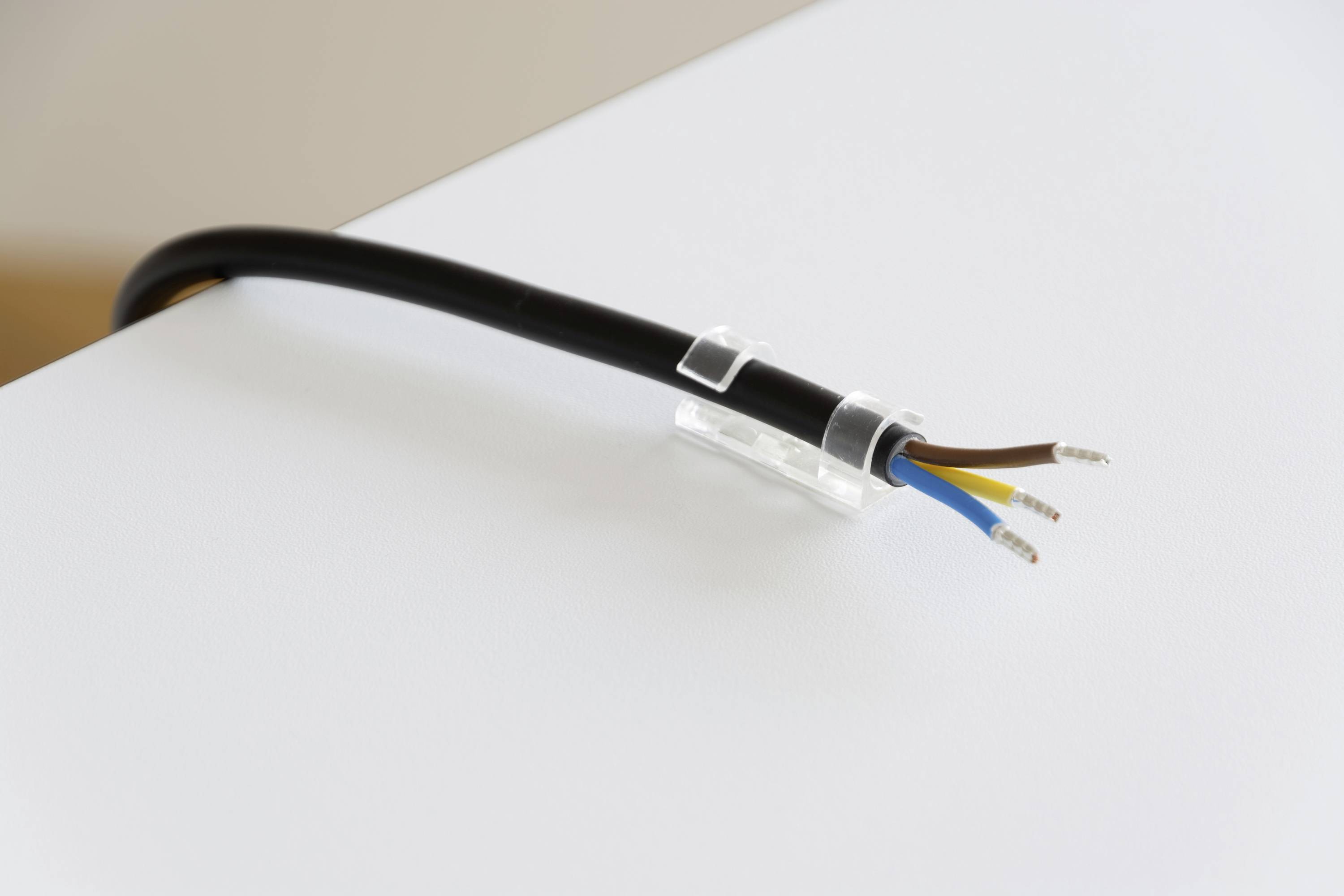 An open cable with black, blue and brown wires is lying on a surface, with the cable secured by a white clip.