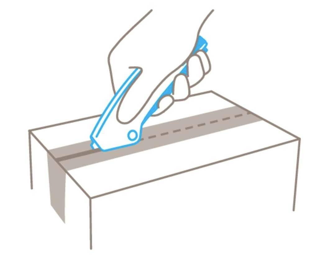 A hand holds a safety knife and carefully cuts along the marked line on a cardboard box.