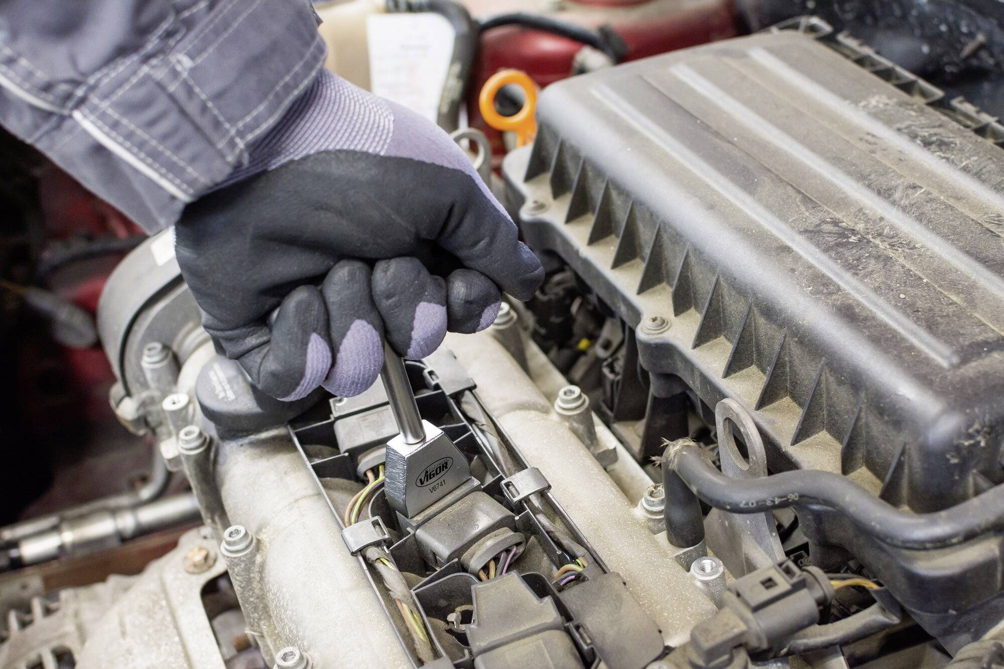 Close-up of a gloved hand using a spanner to work on a car engine component.