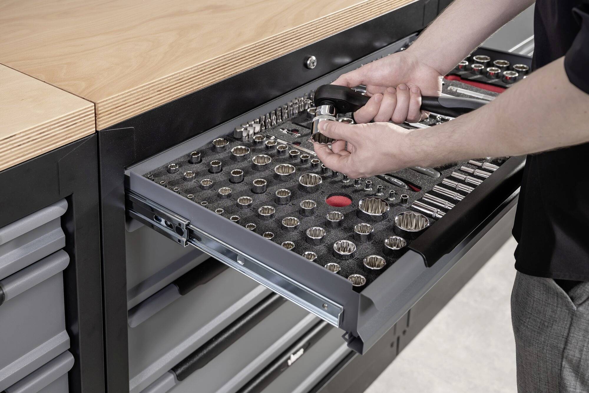 A person opens a drawer with various tools in a workshop. They are holding a spanner in their hand.