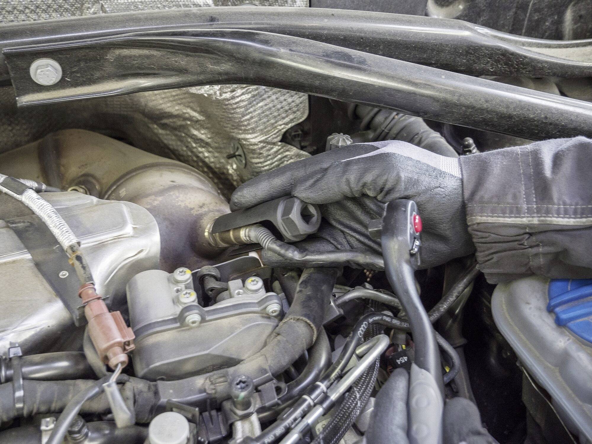 A person wearing black gloves is turning a spanner on a bolt in a car's engine compartment.