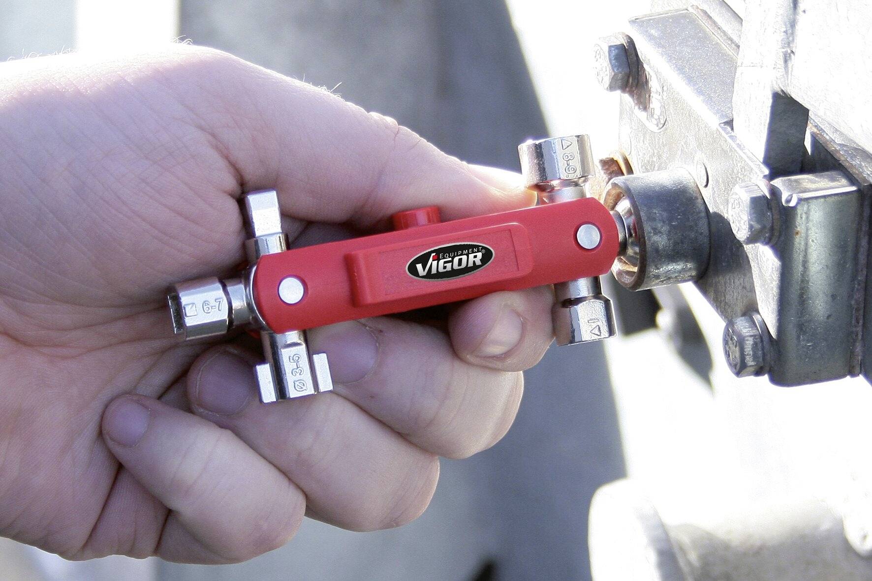 A hand holds a red, multifunctional tool from 'Vigor', being used on a metal connection for fine adjustment.