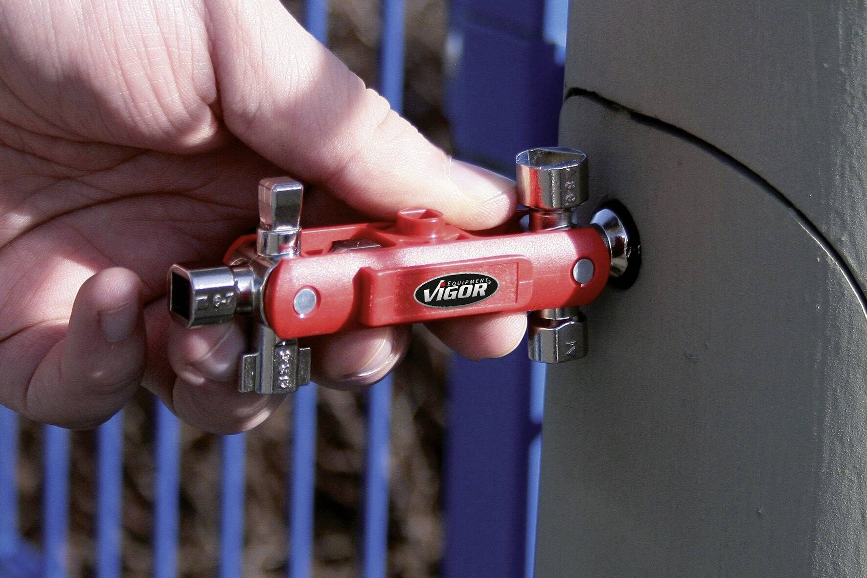 A hand is holding a red square-headed key tool and using it to open a screw on a round container lid.