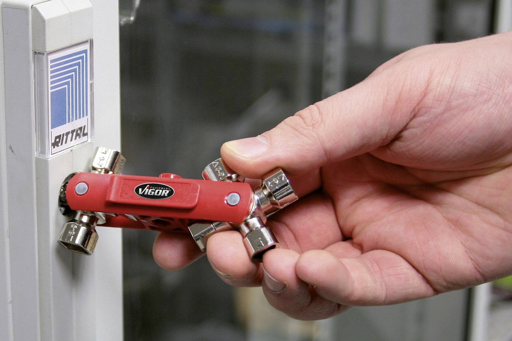 A hand is holding a red tool with multiple keys in front of a cabinet door with a 'Rittal' logo.