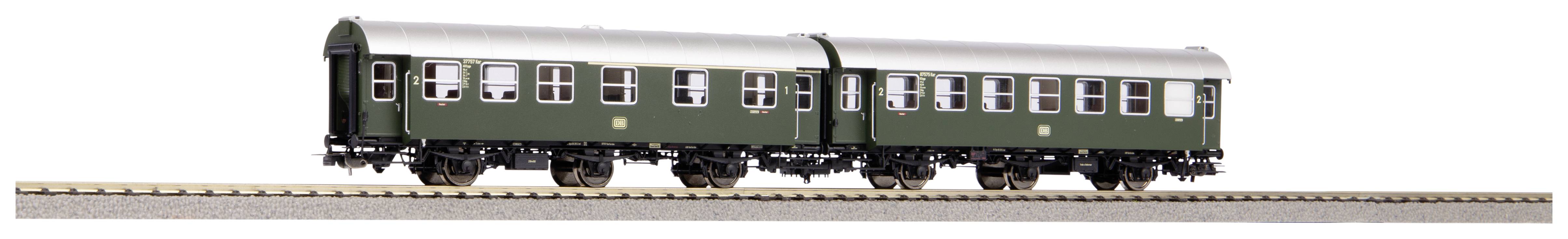 Two green model railway carriages are standing on a section of track. The carriages have multiple windows and silver roofs.