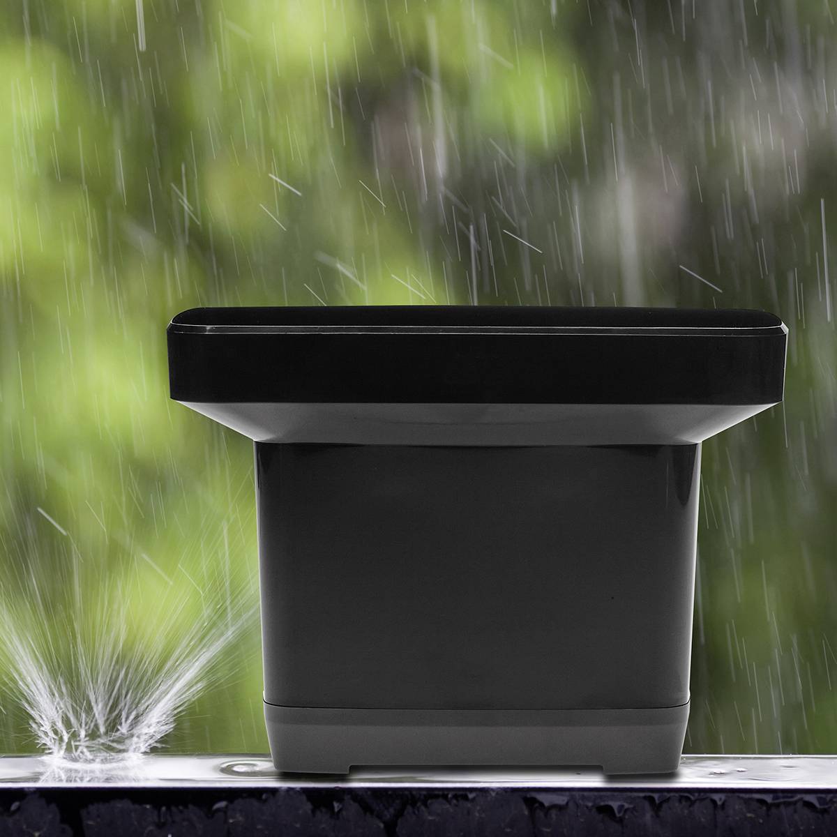 A rain sensor with splashing water outside in front of a blurred green background.