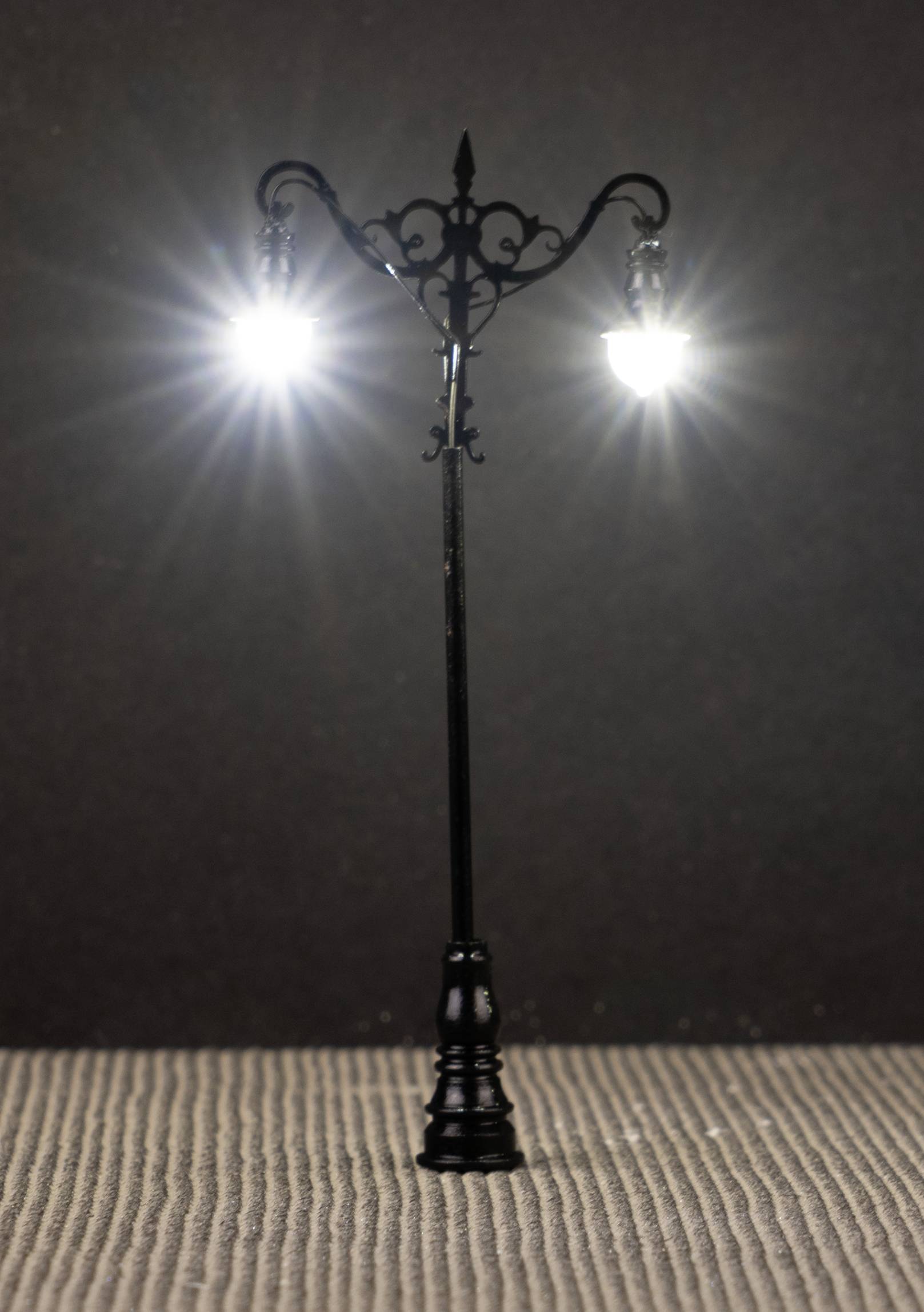 A wrought-iron street lamp with two glowing lamps against a dark background.