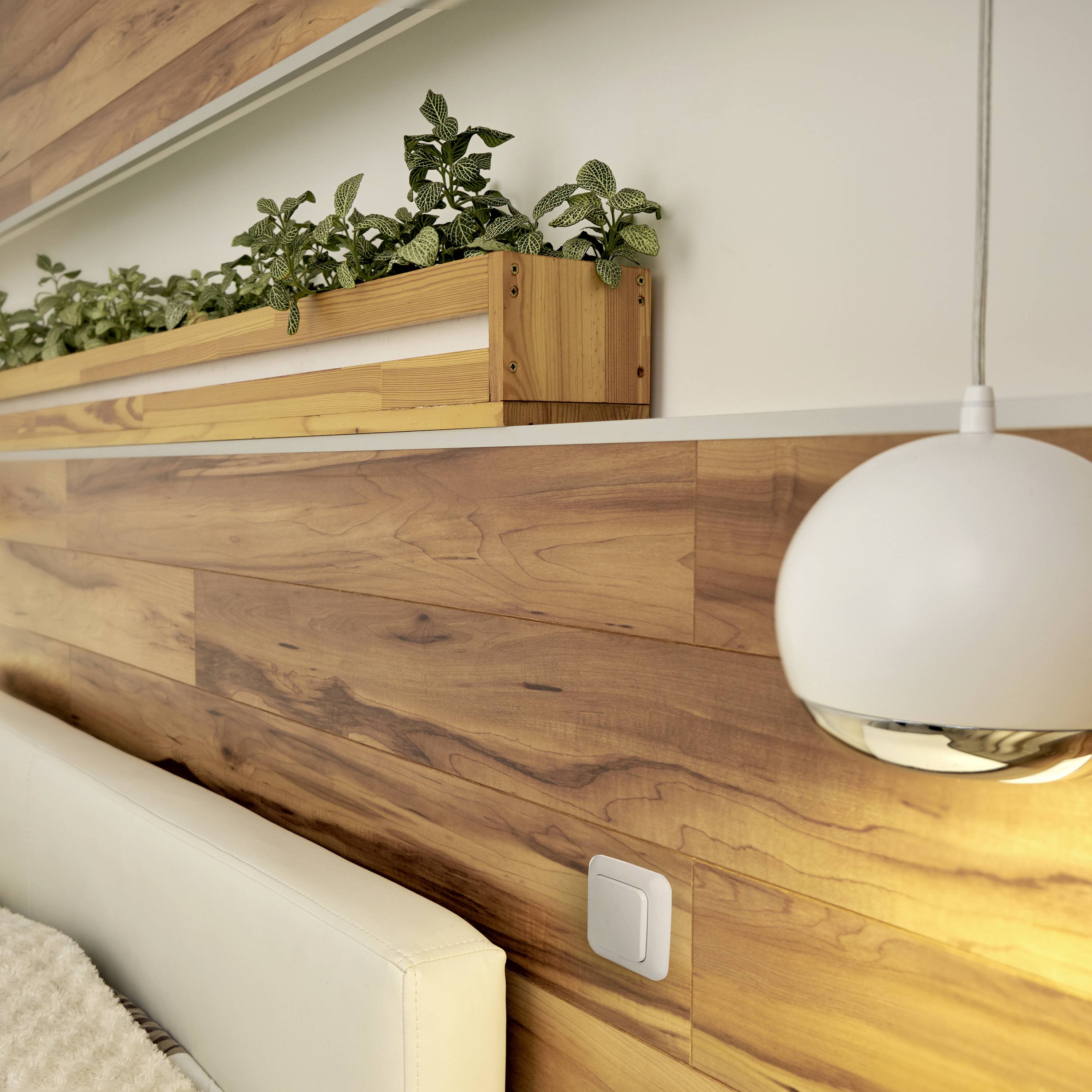 Modern bedroom with wooden panelling and pale wooden furniture. A planter on the wall with green plants.