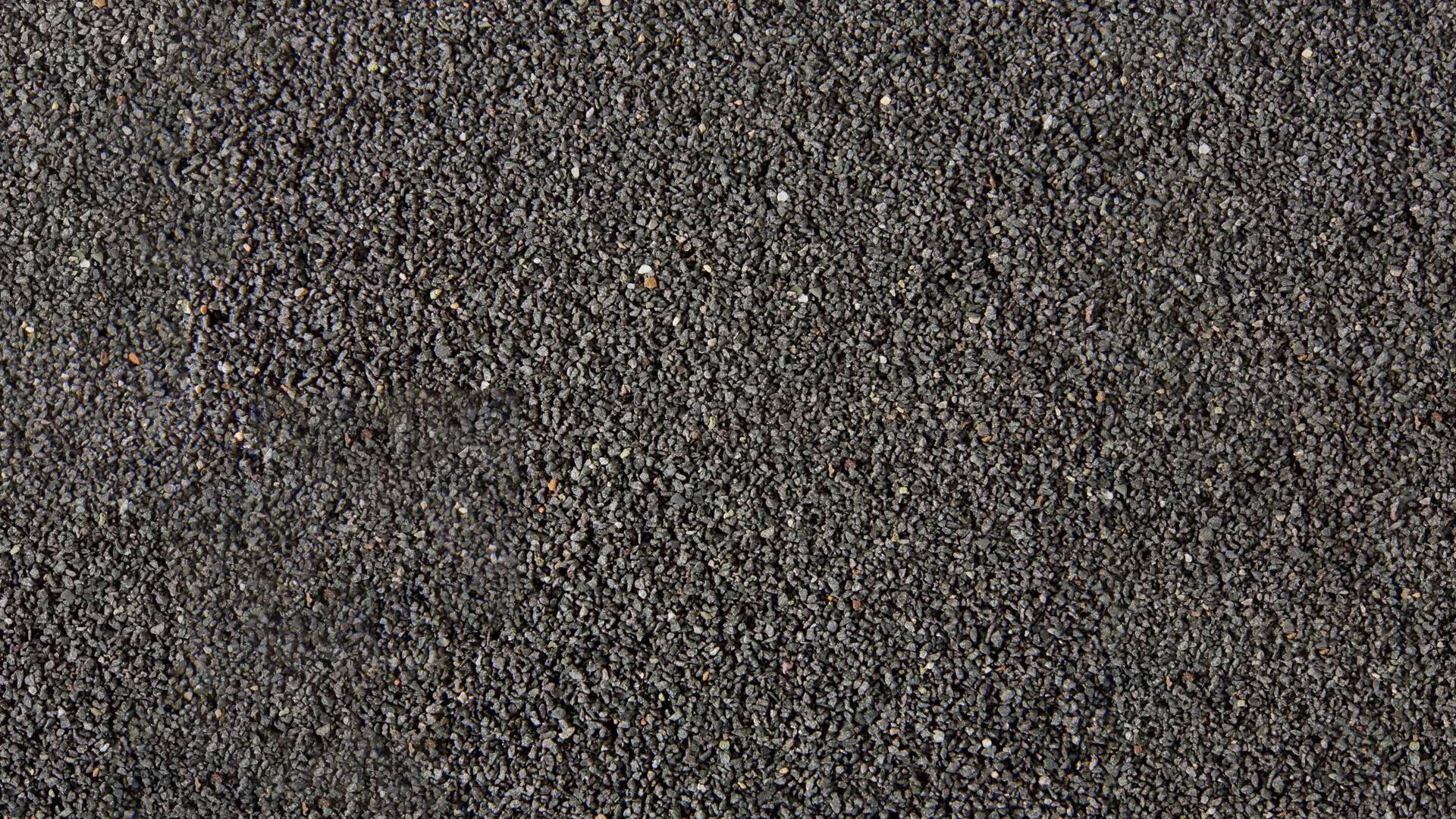 A close-up of black sand, evenly distributed. Texture and colour are the main features of the image, without any visible objects.