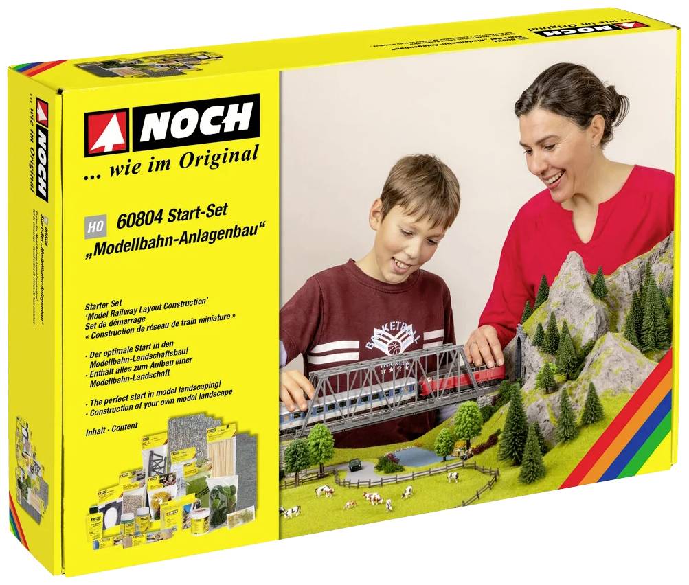 A woman and a boy are building a model railway landscape together. The packaging shows the product and its details.