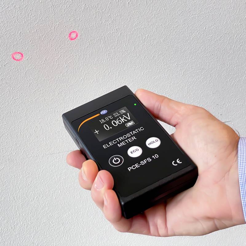A hand is holding an electrostatic measuring device in front of a wall. The device is showing a voltage of 0.06 kV.