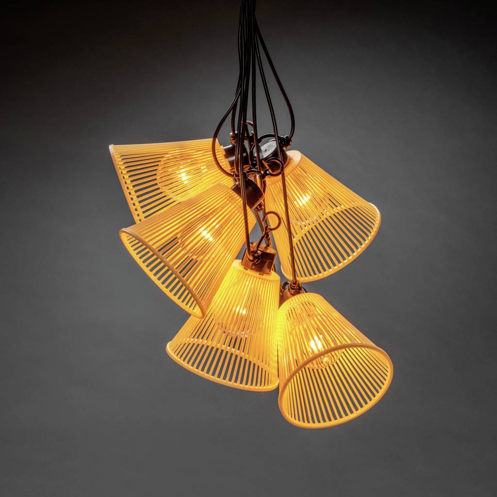 A contemporary hanging light with six orange-glowing shades suspended from black cables, illuminating against a grey background.
