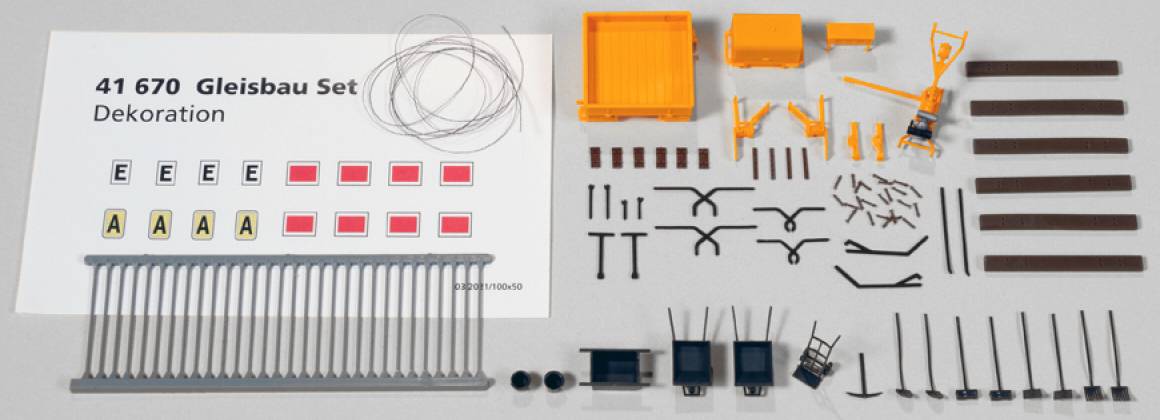 Track-laying set with small model railway components: rails, fences, wires, and small decorative parts.