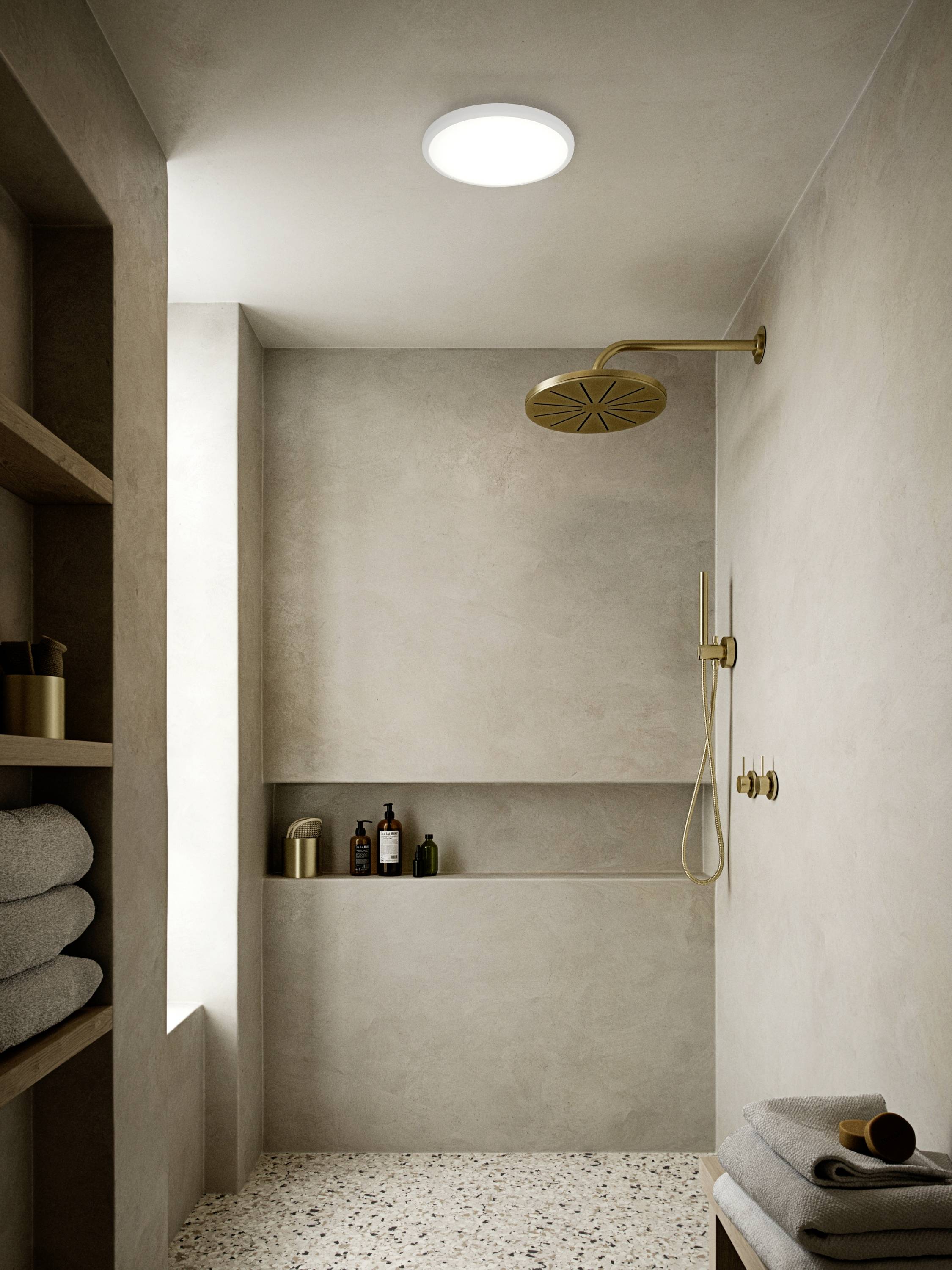 A modern bathroom with an open shower. The light walls and round shower head create a minimalist atmosphere. Towels are placed on the shelf.