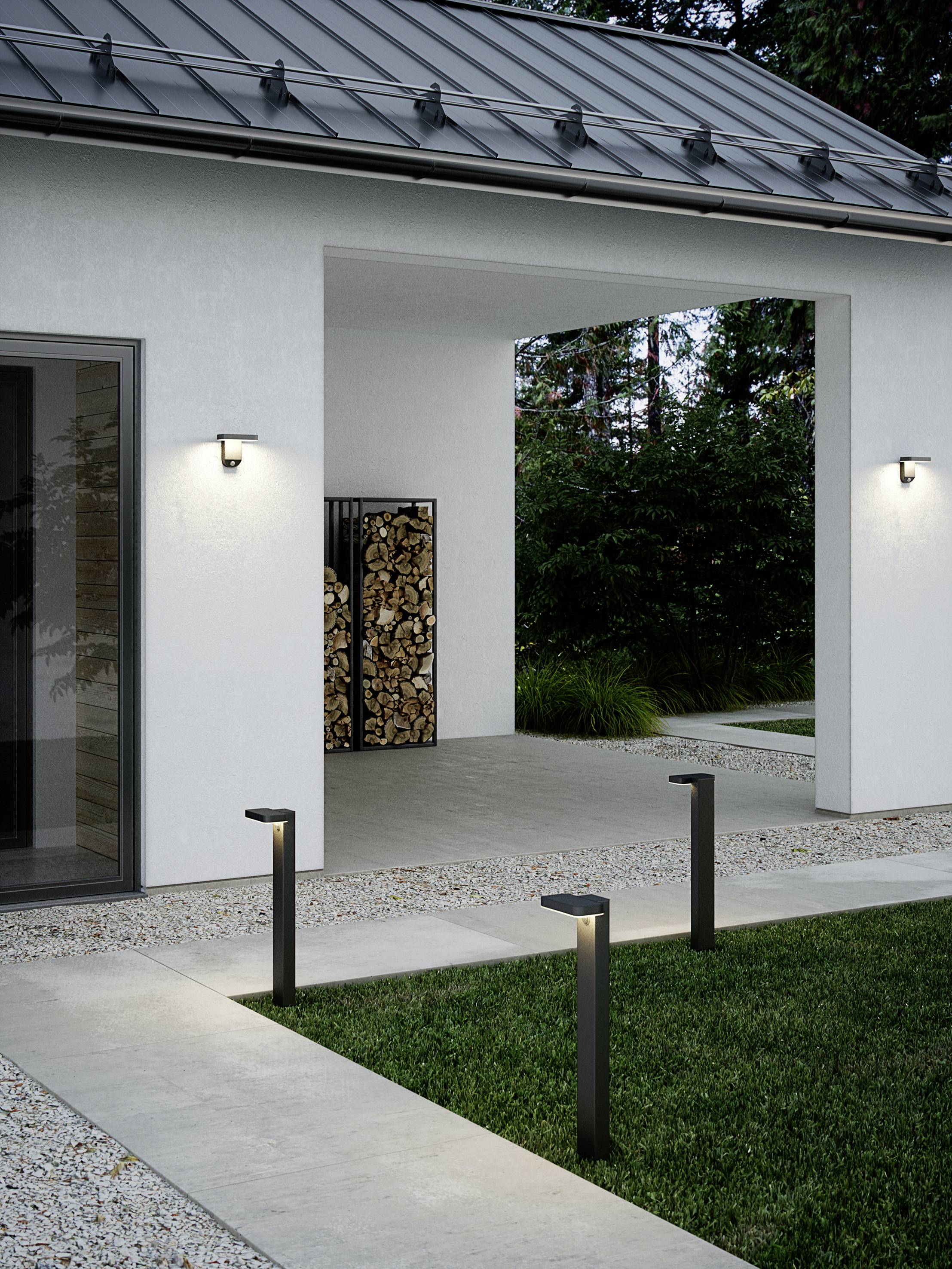 Exterior view of a modern house with a metal roof. Illuminated pathway columns lead to the door, with a wood pile in the background.