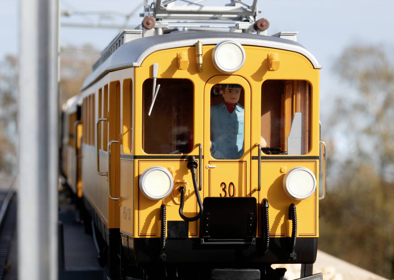 A yellow train with the number 30 travels along a route. At the front, a driver's cab can be seen, with a person sitting inside.