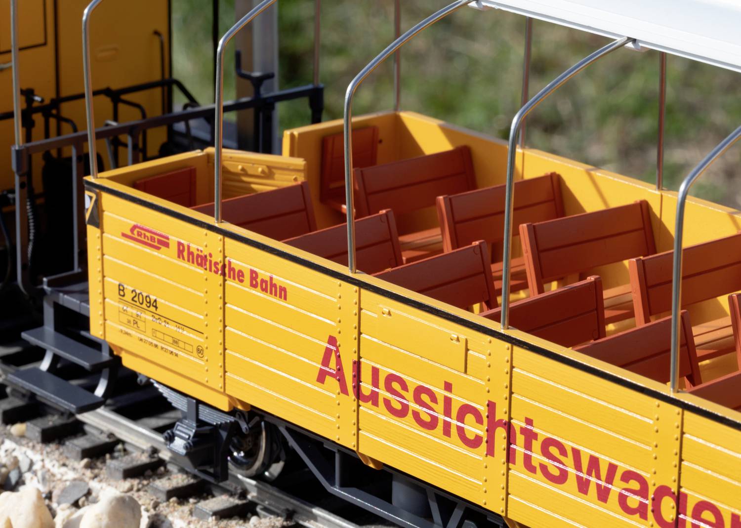 A yellow observation carriage with red seats on a track. On the side it reads 'Rhaetian Railway' and 'Observation Carriage'.