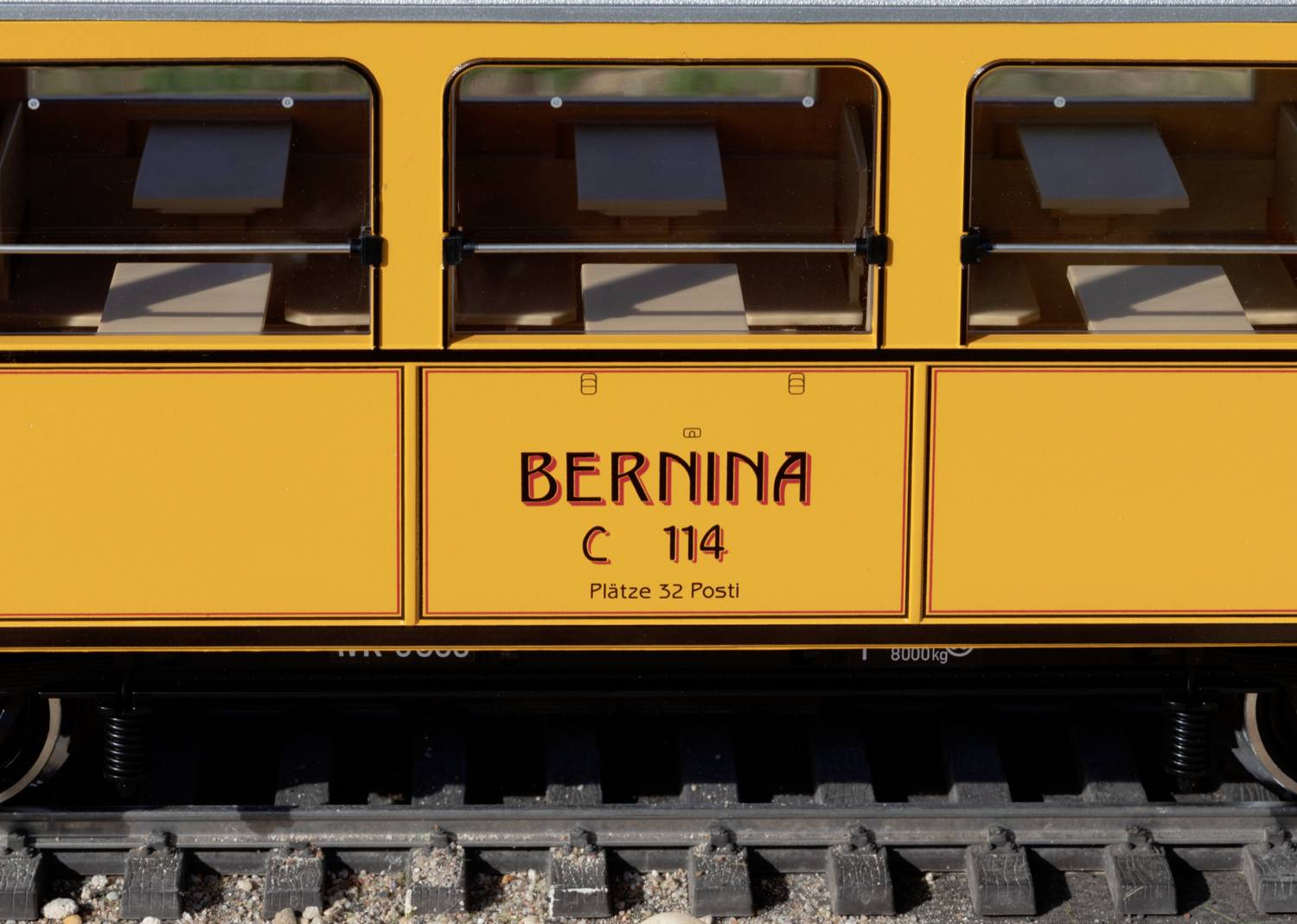 A yellow railway carriage with the inscription 'Bernina C 114, Plätze 32 Posti'. The carriage is standing on railway tracks.