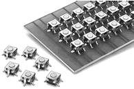 Small, square switches arranged with four pins on a board, with some switches lying loose beside it.
