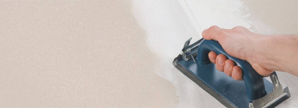 A person is spreading white plaster evenly on a wall with a trowel.