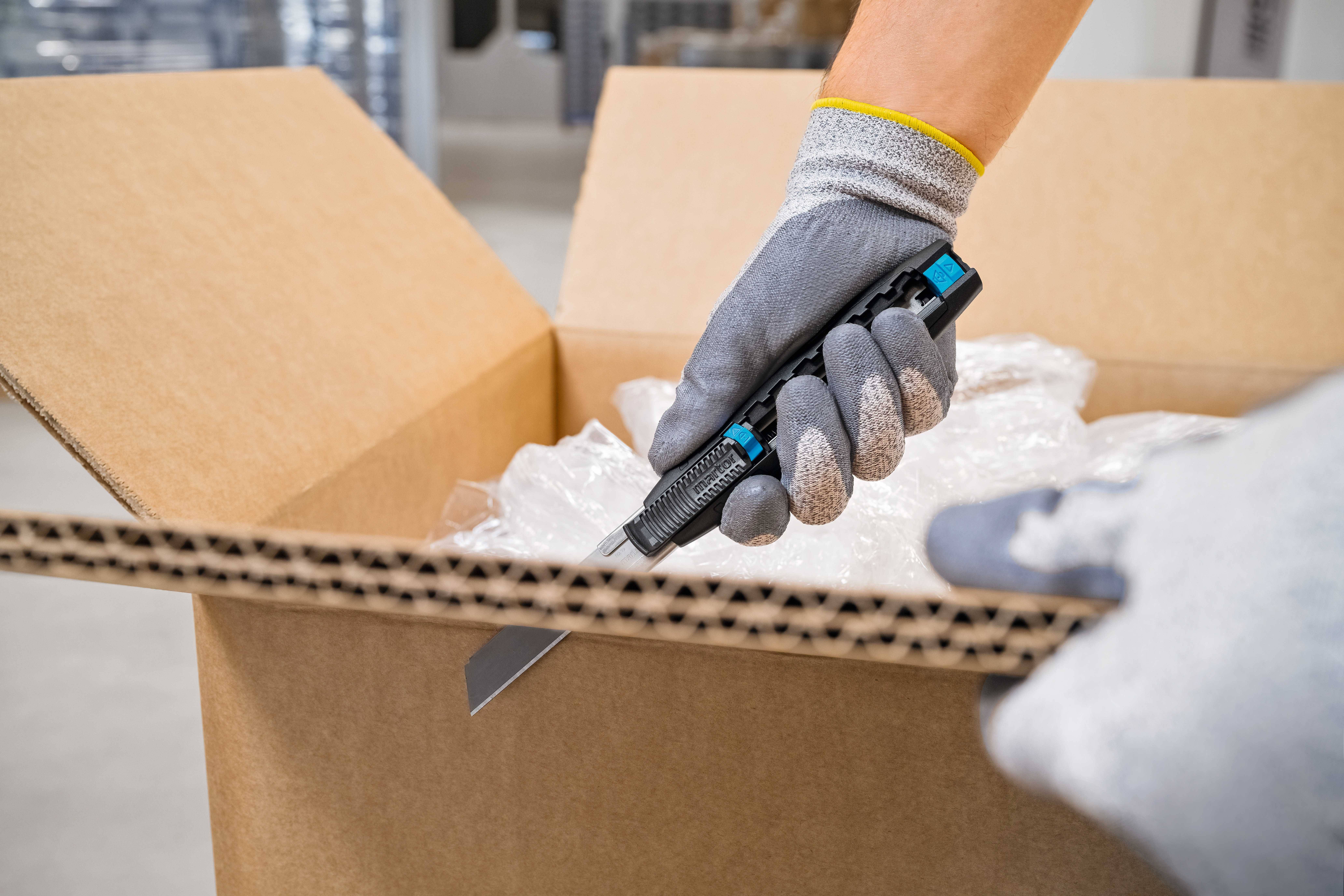 A person carefully opens a cardboard box with a craft knife. The box contains bubble wrap.