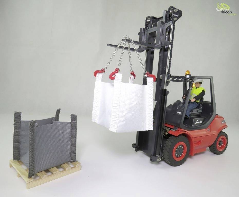 A model forklift is lifting white, empty bulk bags with a chain next to a grey box on a pallet. A worker is seated in the driver's seat.