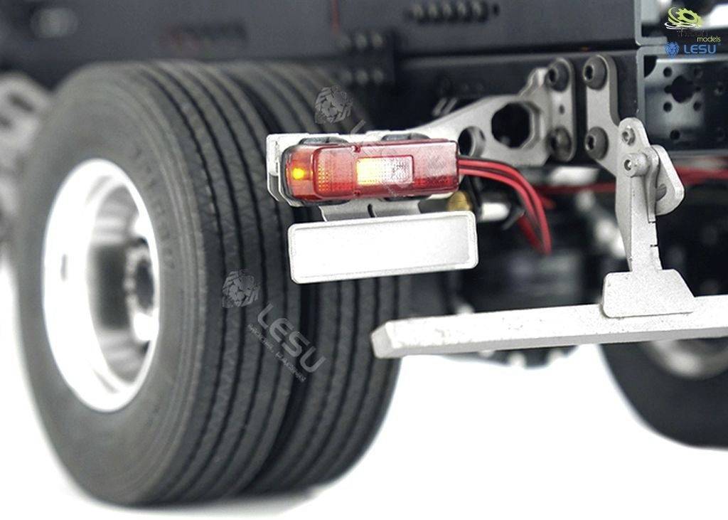 Lorry rear light with red and white lenses, mounted on a metallic frame in front of a large tyre.