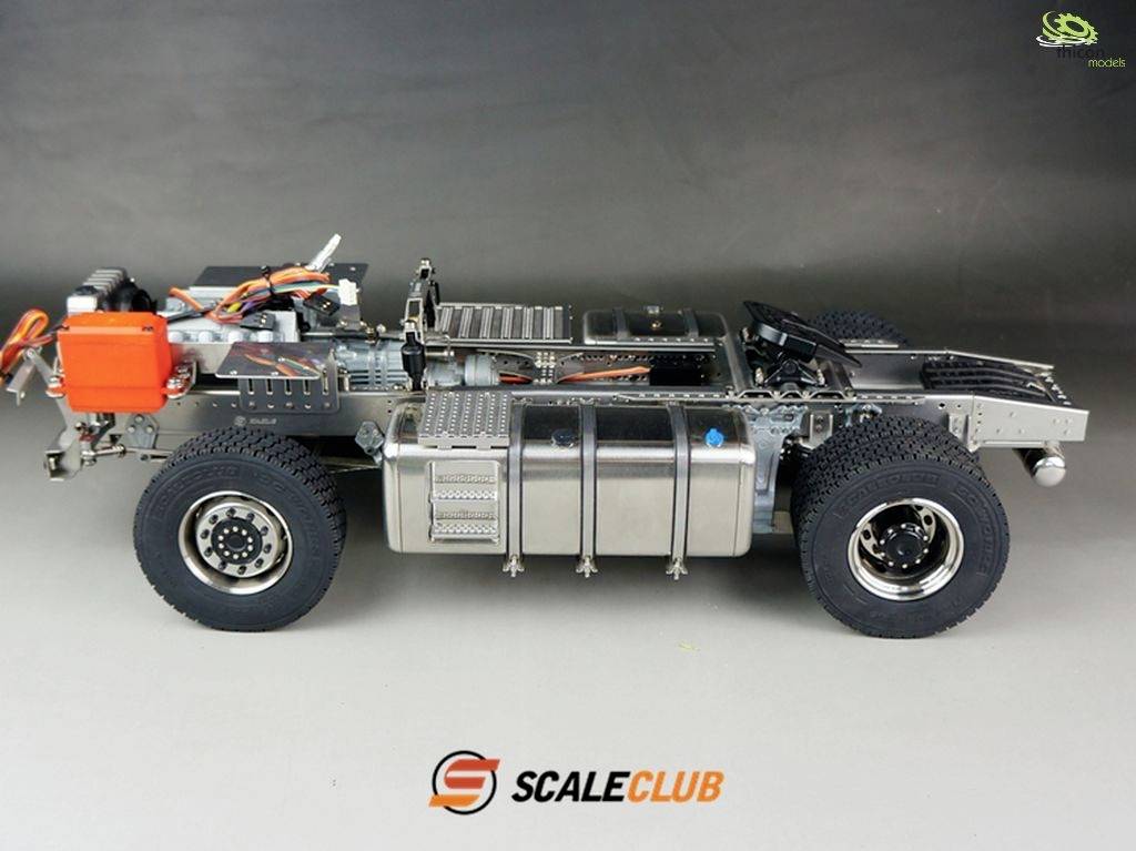 Long, metallic model vehicle frame with visible technical components and cables. Wheels are fitted. ScaleClub logo at the bottom.