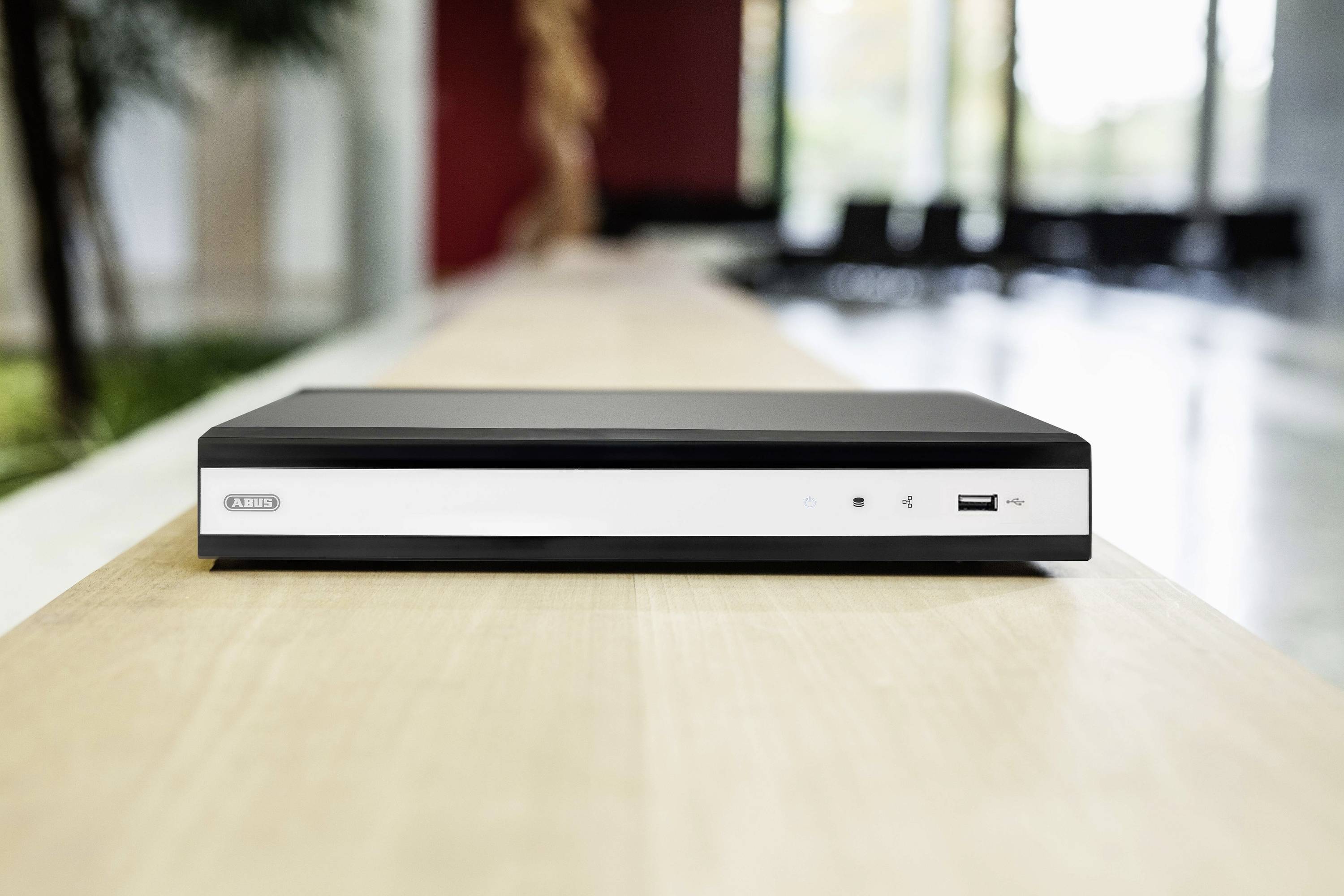 Pictured is a black electronic device with a flat form. It is standing on a wooden table in a modern interior.