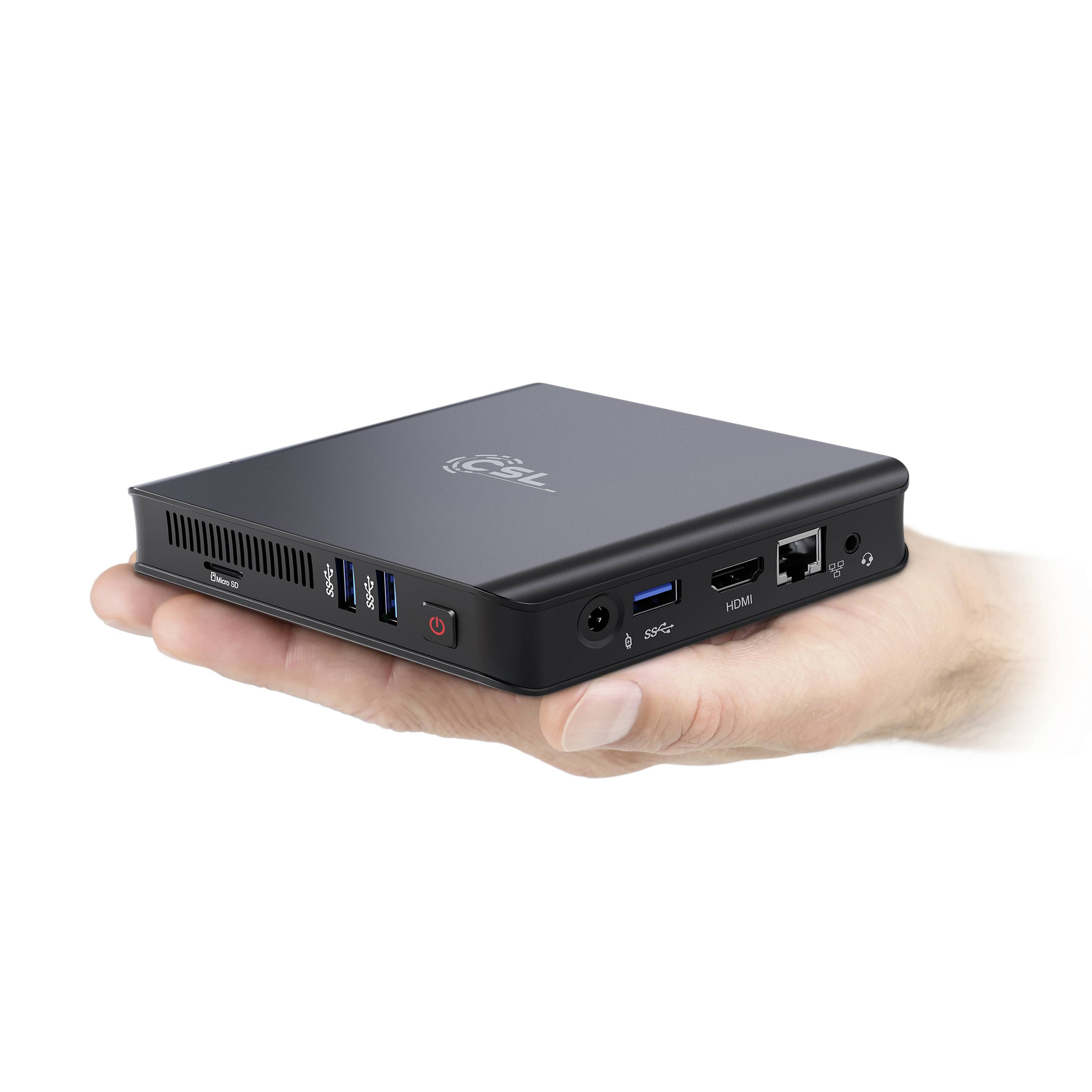 A hand is holding a small, black computer with multiple ports, including USB and HDMI connections.