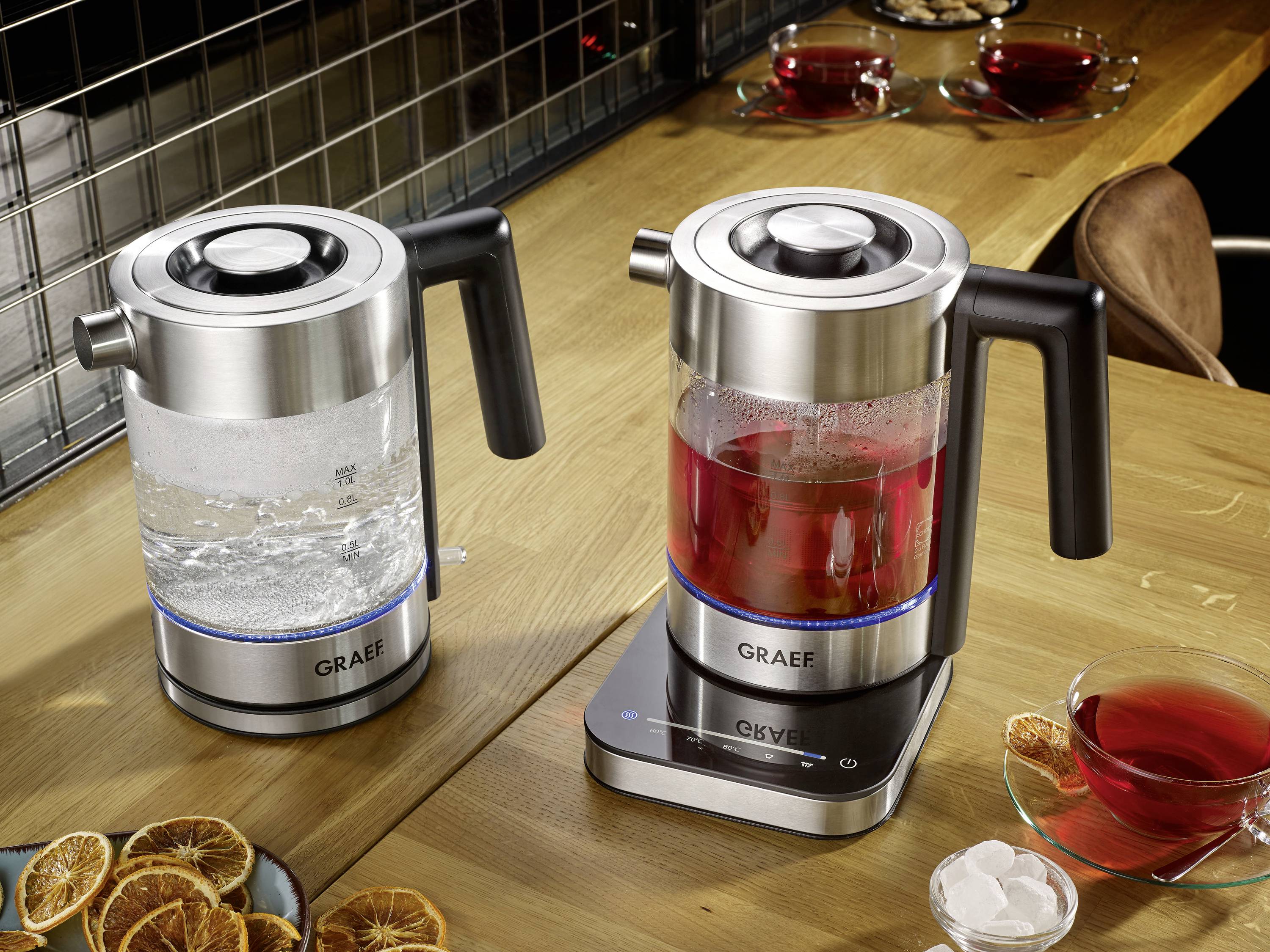 Two grey kettles, with the one on the left containing boiling water and the one on the right holding red tea, placed on an electronic hot plate.