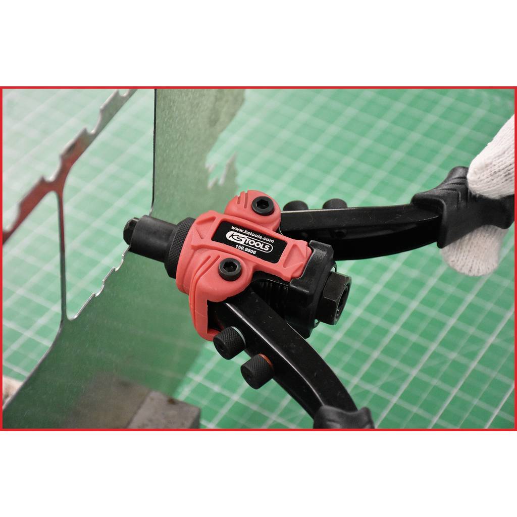 A red hand tool pliers cuts a piece of wire against a green background. A gloved hand holds the pliers.
