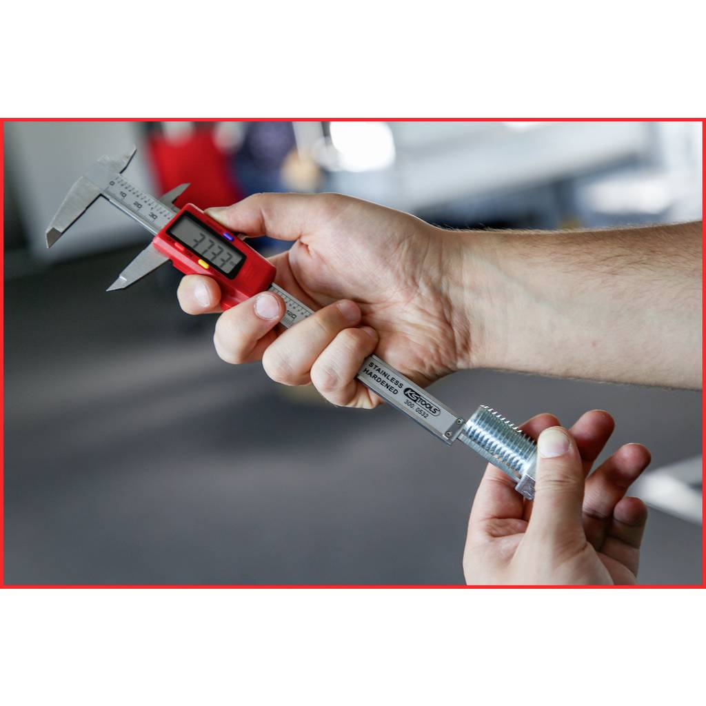 A person is measuring a metal part with a digital calliper. The calliper shows 34.22 mm. The surroundings appear industrial.