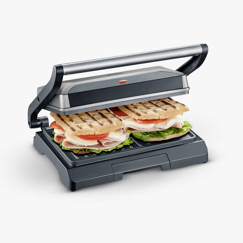 An electric Panini grill with two Panini sandwiches containing ham, tomatoes, lettuce, and melted cheese.