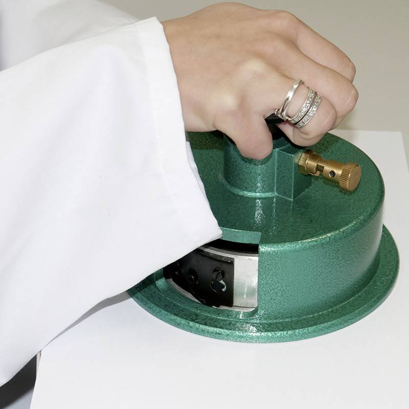 A hand in a white laboratory coat is holding a green piece of laboratory equipment. The person is wearing several rings.