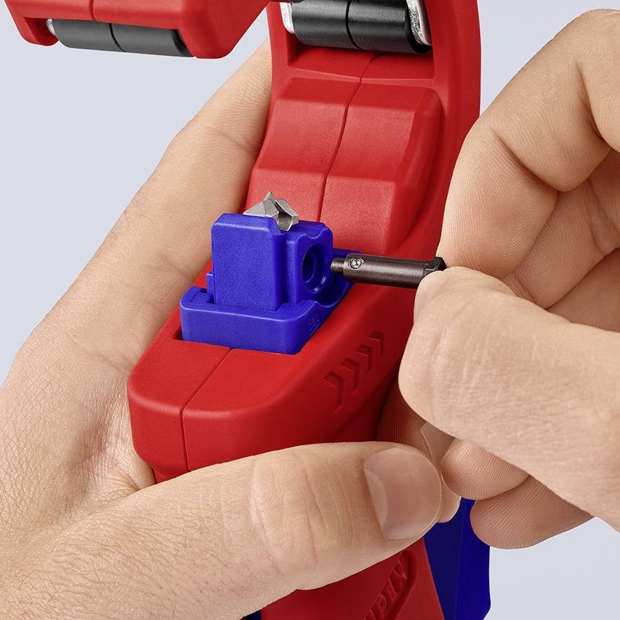 Red cable wire stripping pliers with a blue adjustment mechanism, being held in one hand. A pencil is placed in the pliers.