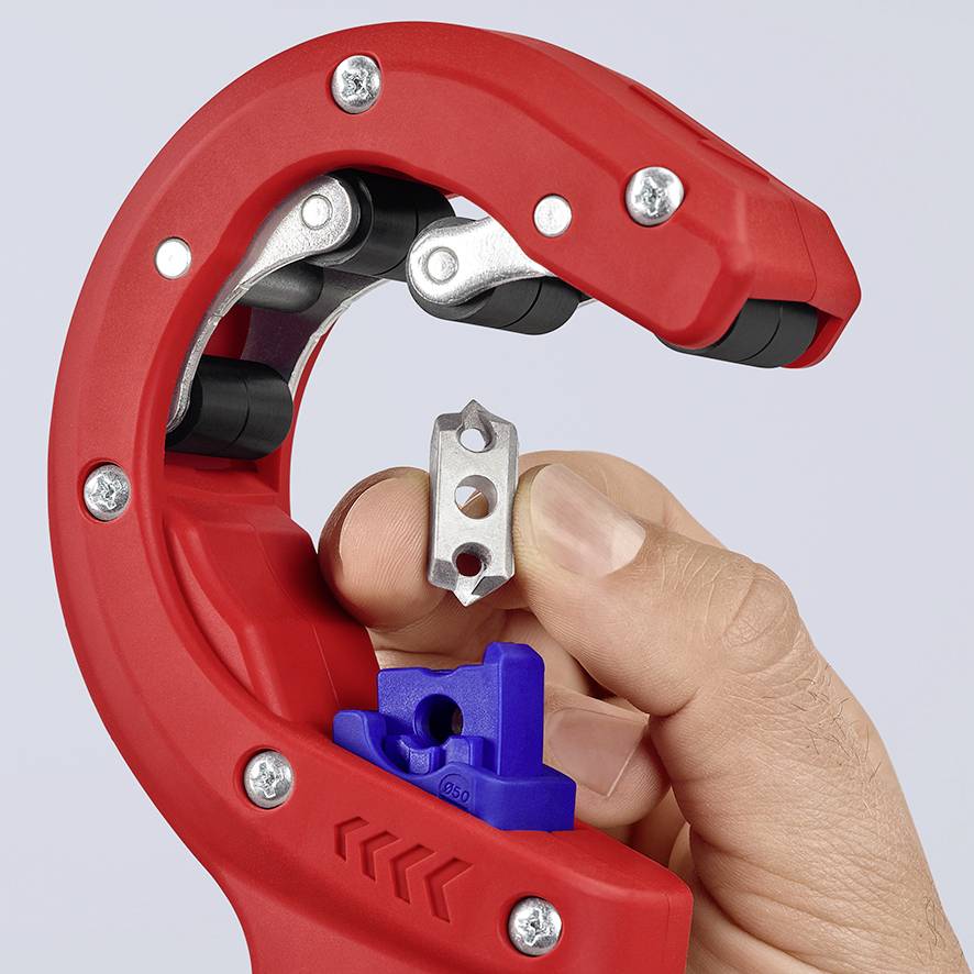 A hand is holding a small metal part in front of a red pipe cutter, which is used for cutting pipes.