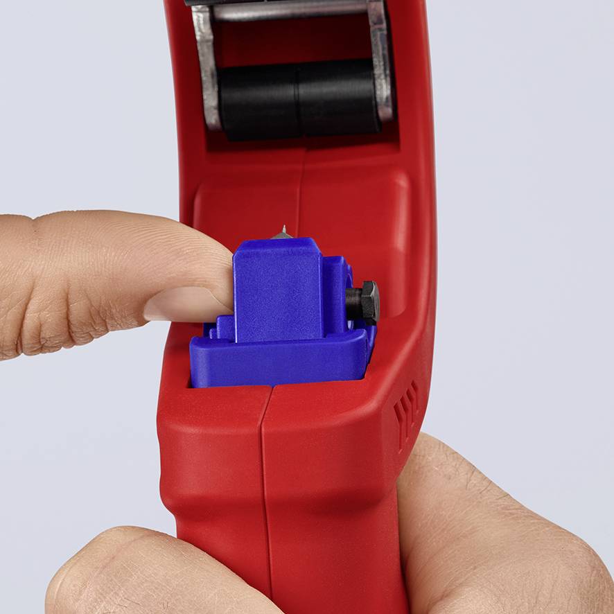 A hand is holding a red labeller and pressing the blue lever to print a label.