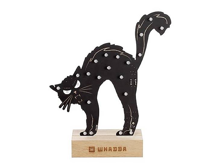 A black cat figurine with an arched back stands on a wooden base. It is adorned with white spots.