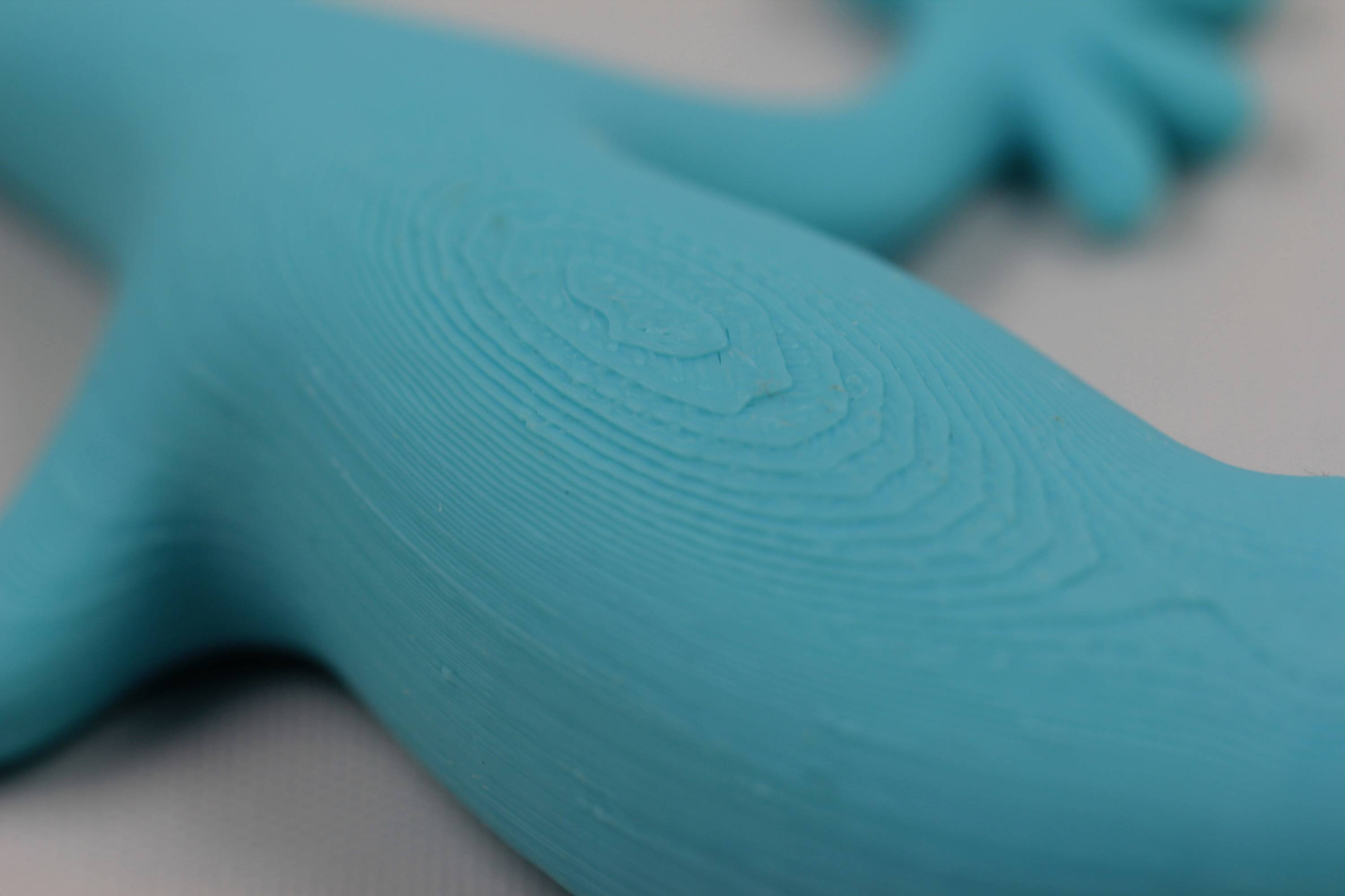 Close-up of a blue plastic toy in the shape of a lizard. The material shows fine, concentric lines on the surface.