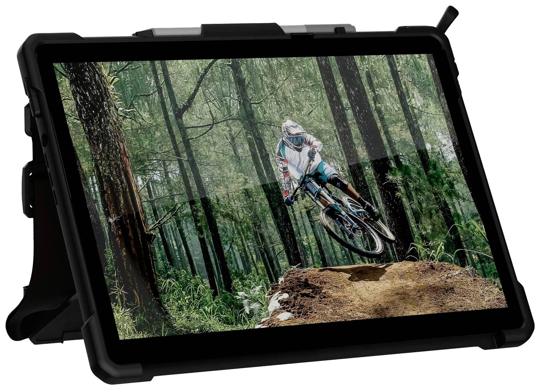 A mountain biker in colourful clothing rides over an elevation in a dense, green forest. The image captures an exciting action shot.