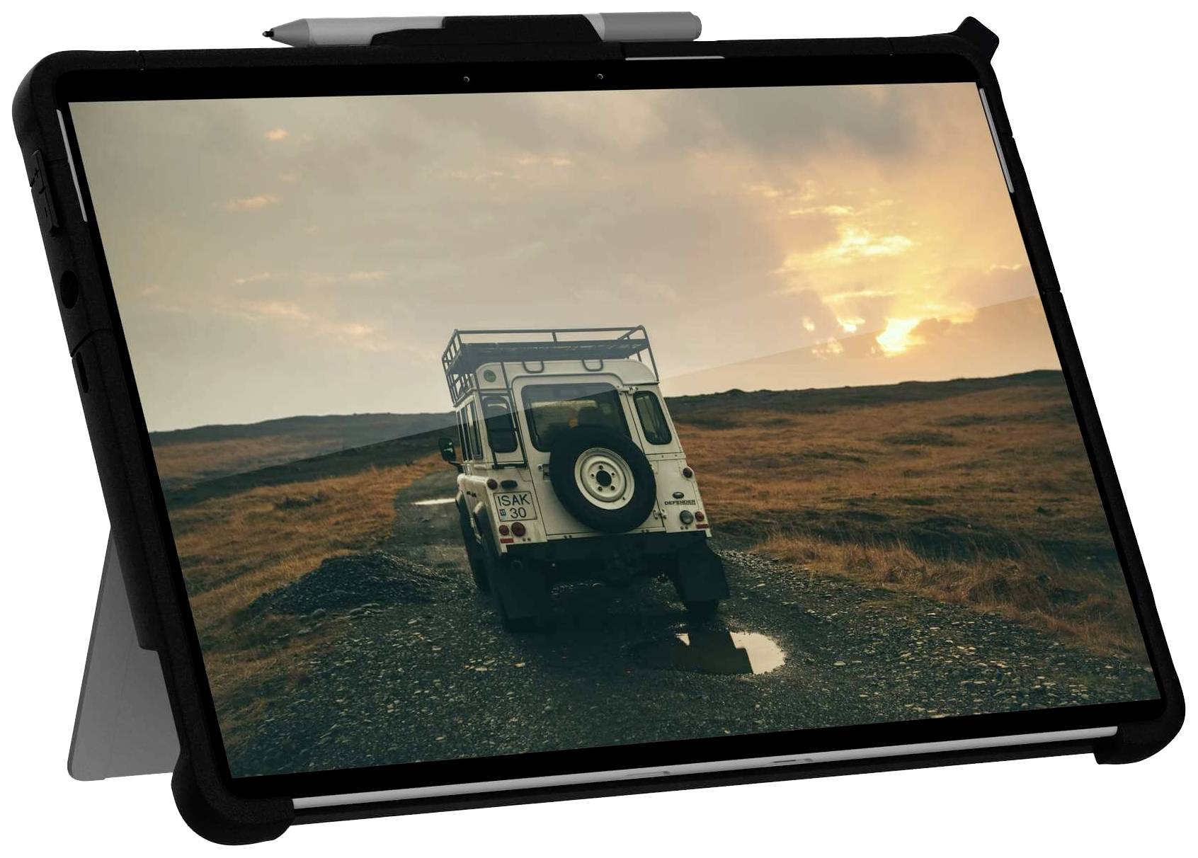 A tablet displays a photo of an off-road vehicle on a narrow path in a barren landscape at sunset.