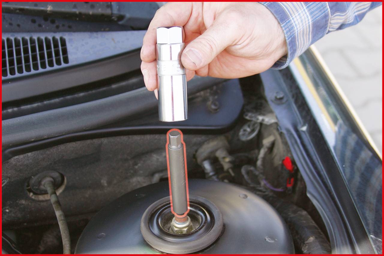 A hand holds a spark plug over an open engine, ready to install it. A person is working on a vehicle engine outdoors.