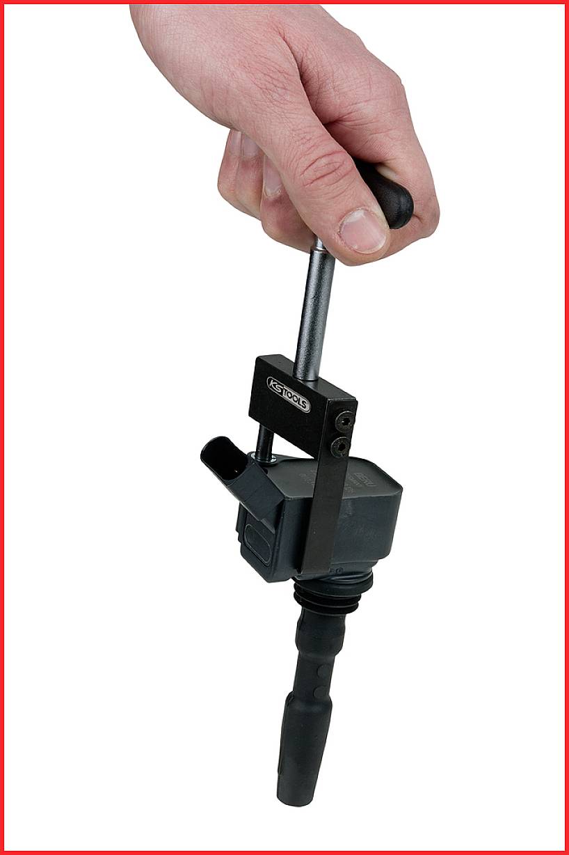 A hand is holding a tool for assembling ignition coils. The tool is black and is designed for safe installation or removal.