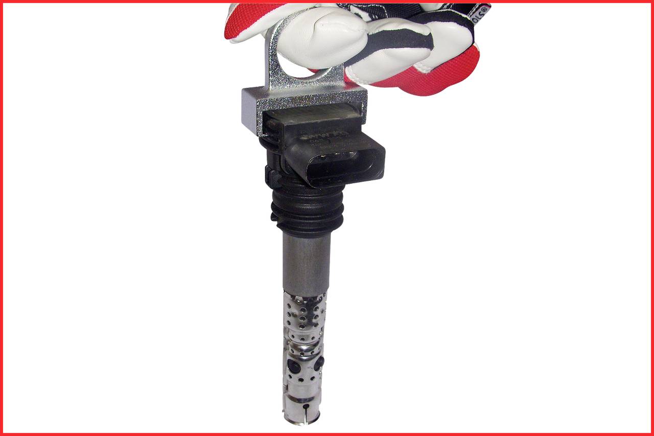 A hand in a glove holds an ignition coil for a car.